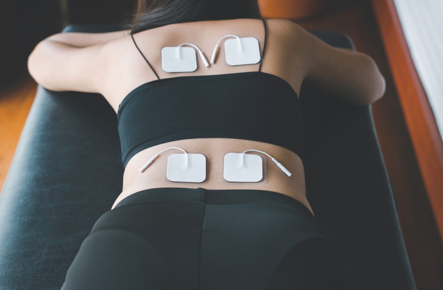physical-therapy-for-woman-patient-with-tens-electrode-pads-on-backpreparing-equipment-1536x1008 Tens